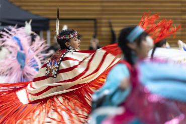 Indigenous women in colourful, traditional clothign are seen dancing at the powwow