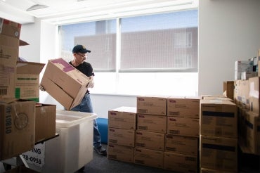 A worker lifts boxes of personal protective equipment supplies amidst stacks of other boxes