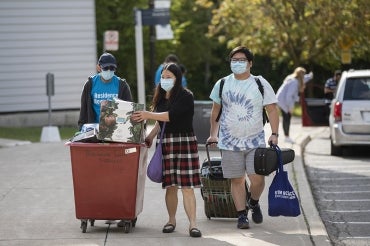 a pair of students, helped by a volunteer, bring their belongings to residence at UTM