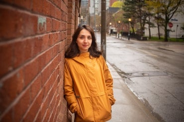 Azadeh Barzideh stands outside her residence, wearing a yellow raincoat