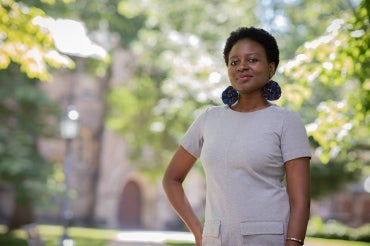 Nadège Compaoré stands on campus with trees and a stone building in the background