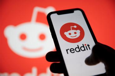 A person hold a cellphone with the reddit logo visible