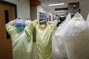 Two doctors don PPE as they walk down a hospital corridor