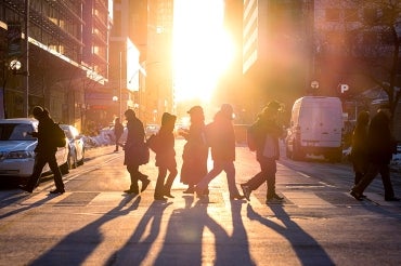 People crossing the street as the sun sets.