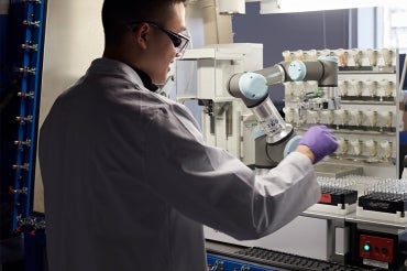 Researcher removes a vial of pre-dispensed reagent from an automated solid dispensing robot 