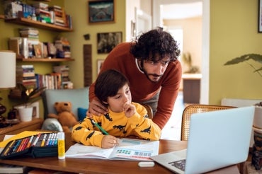 a father and son look at a laptop screen together while the son does is homework