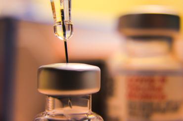 Close-up of a needle drawing vaccine from a bottle