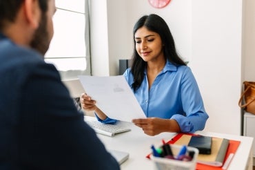 a woman looks over a resume while the candidate looks on