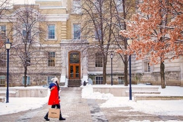 a female student in a red coat walks past a snow-dusted Sanford Fleming building at U of T st george campus