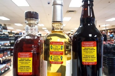 3 bottles of various types of alcohol at a Whitehorse liquor store with yellow and red health warning stickers