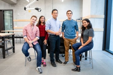 Chris Yip poses in an engineering lab with four Pearson Scholars