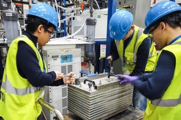 Members of the CERT team wearing blue hard hats and yellow vests work on pilot-scale electrolyzer equipment equipment