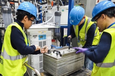 Members of the CERT team wearing blue hard hats and yellow vests work on pilot-scale electrolyzer equipment equipment 