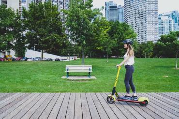 A woman rides a Roll brand e-scooter in Toronto along the boardwalk downtown