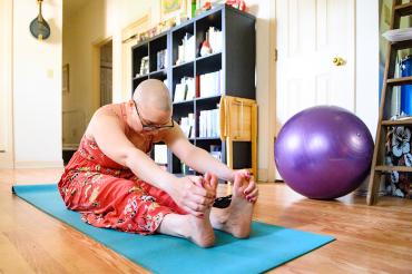 bald woman is doing yoga in her living room