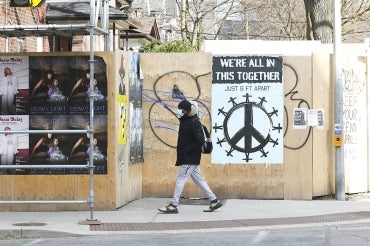 A solitary man walks past a sign in Parkdale, Toronto that reads "we're all in this together"