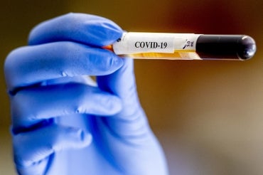 a gloved hand holds up a vial of blood that has a covid-19 label