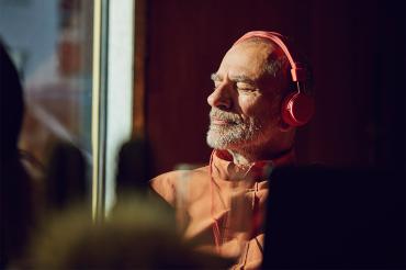 older man listens to music with eyes closed by a sunny window