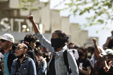 A young Black woman raises her fist in the air at a Black lives matter protest