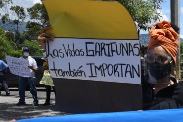 A Garifuna woman hold a sign that reads Las Vidas Garifunas tambien importante