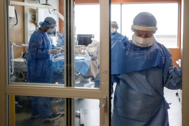 nurses attend to a covid-19 patient in a toronto hospital. one of the nurses looks tired and is leaving the room