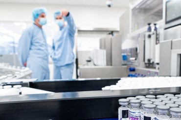 two workers in the background of a vaccine production line