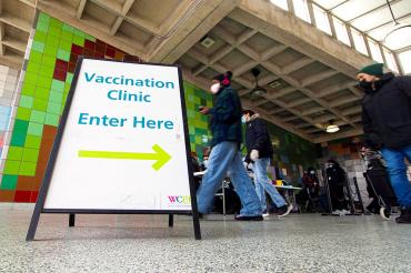 people walk past a sign that reads "vaccination clinic enter here"