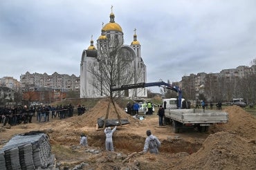 a crane lifts a body out of a mass grave in Bucha, Ukraine