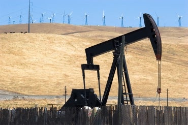 an oil drill in the foreground with a row of wind turbines in the background