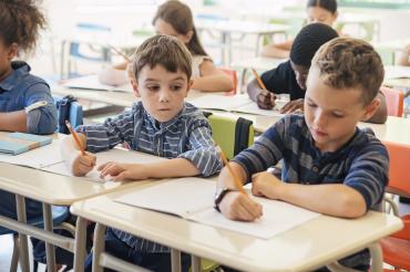 A child peers at another child's work in a classroom