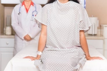 a woman in a medical gown sits on an examination table and a female doctor stands behind her