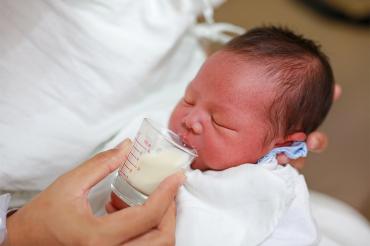 newborn baby being fed milk in a cup