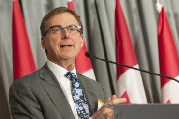 Tiff Macklem speaks at a lecturn with Canadian flags in the background