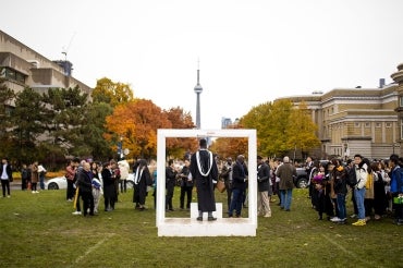 A person is posing in a large photo frame with the CN Tower is in the background