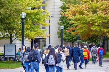 Many students walking in front of Roberts Library with fall foliage visible