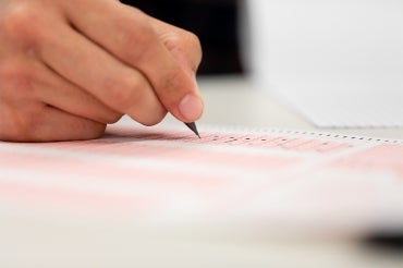 Close up photo of a hand holding a pen above a multiple choice test sheet