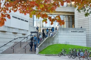 Students walk into Robarts Library with a tree in the foreground