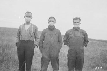 Three men stand in a field in alberta wearing gauze masks