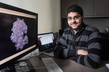Ali Punjani sits in front of a computer displaying a protein image