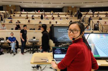 Cherry Ng sits at the head of a lecture hall and is turned to the camera