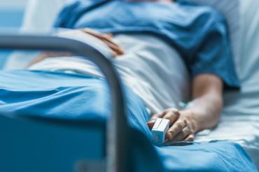 Person lying down in a hospital bed with a monitor on their finger