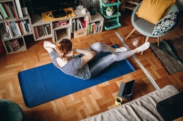 woman doing crunches on a yoga mat in her living room with tablet beside