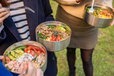 people hold Inwit's reusable takeout containers filled with food while eating in the park