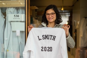 Laura Smith holds up a lab coat with her name and the planned year of her PhD thesis defence 