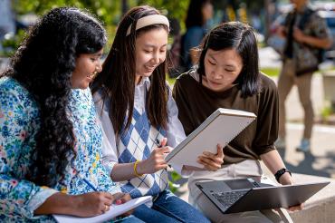 three students seated together working together on a project outdoors