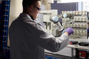 Researcher removes a vial of pre-dispensed reagent from an automated solid dispensing robot 