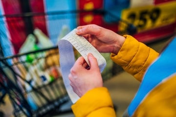 Woman looks at a grocery shopping receipt with a full shopping cart in the background