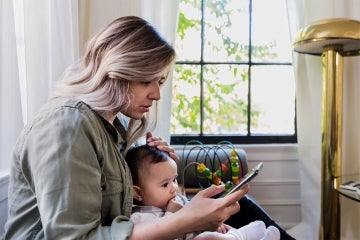 Mother looking at a cellphone while taking care of infant son