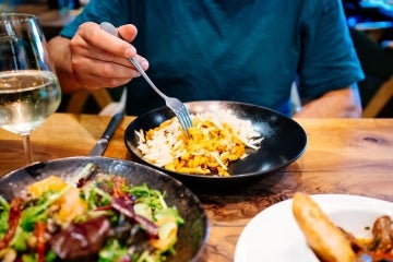 man eating a big bowl of pasta, wine and salad