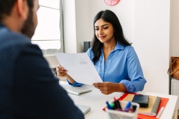 a woman looks over a resume while the candidate looks on